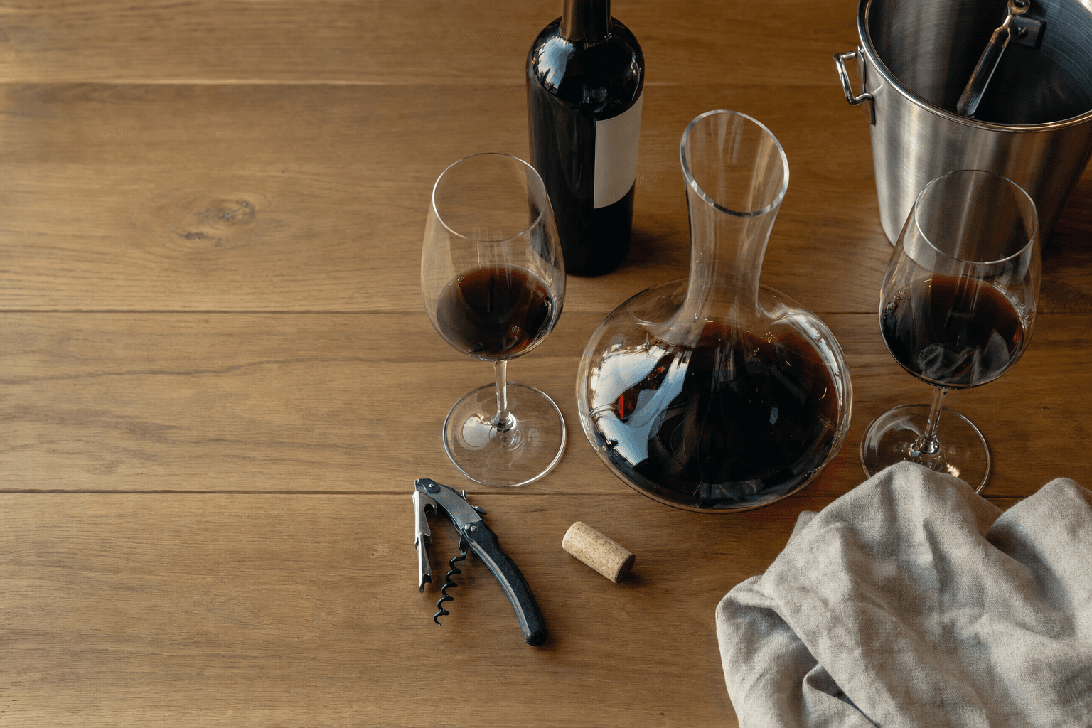 Accesorios de vino — copas, decantador y sacacorchos sobre una mesa de madera