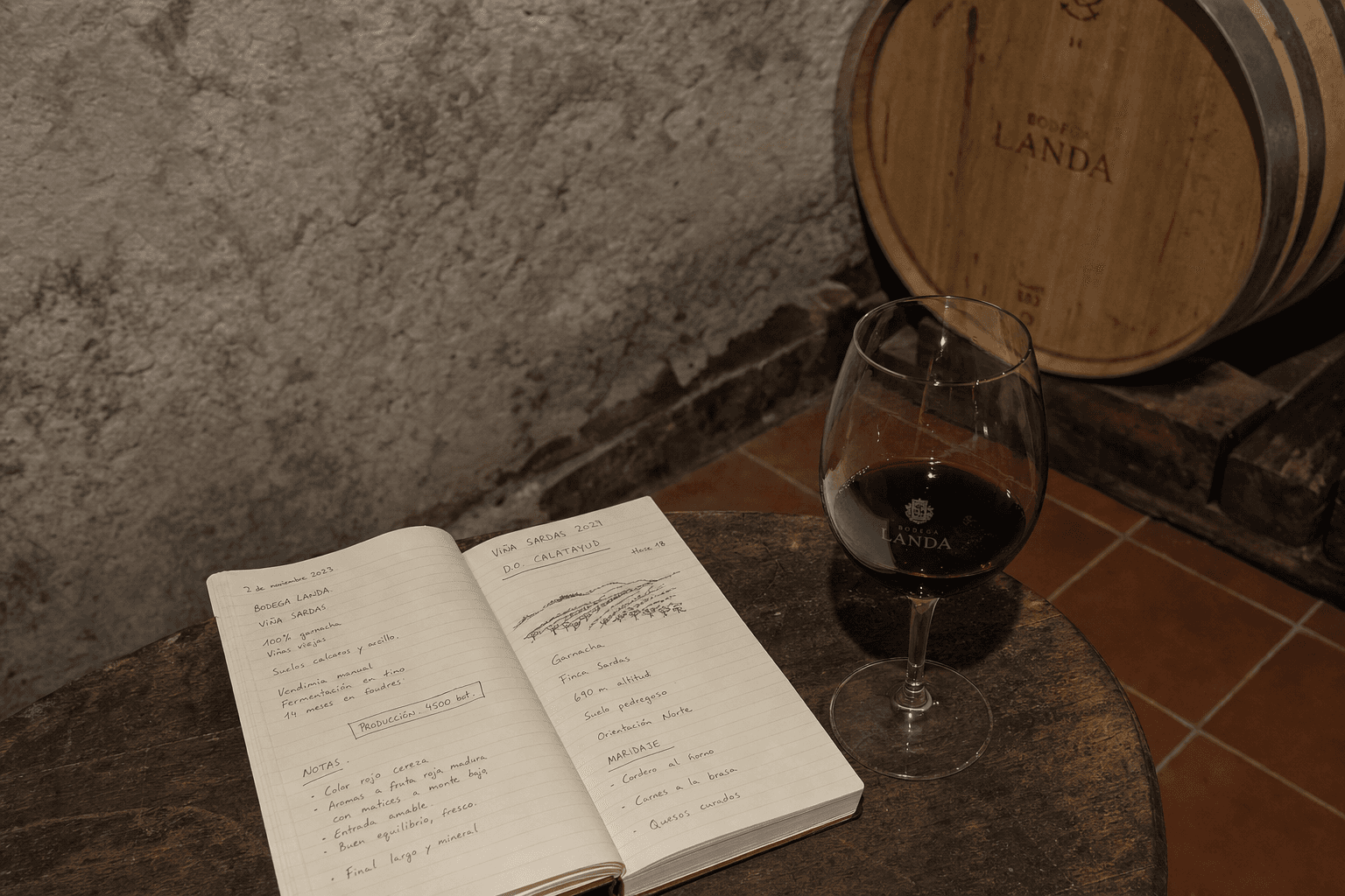 Bodega castellana con barricas, cuaderno de notas y copa al fondo